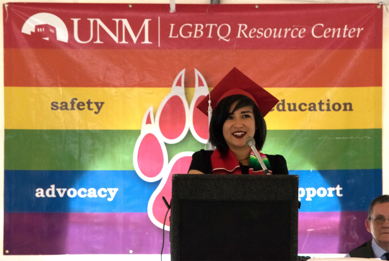 Grad standing at a podium in front of the LGBTQRC banner